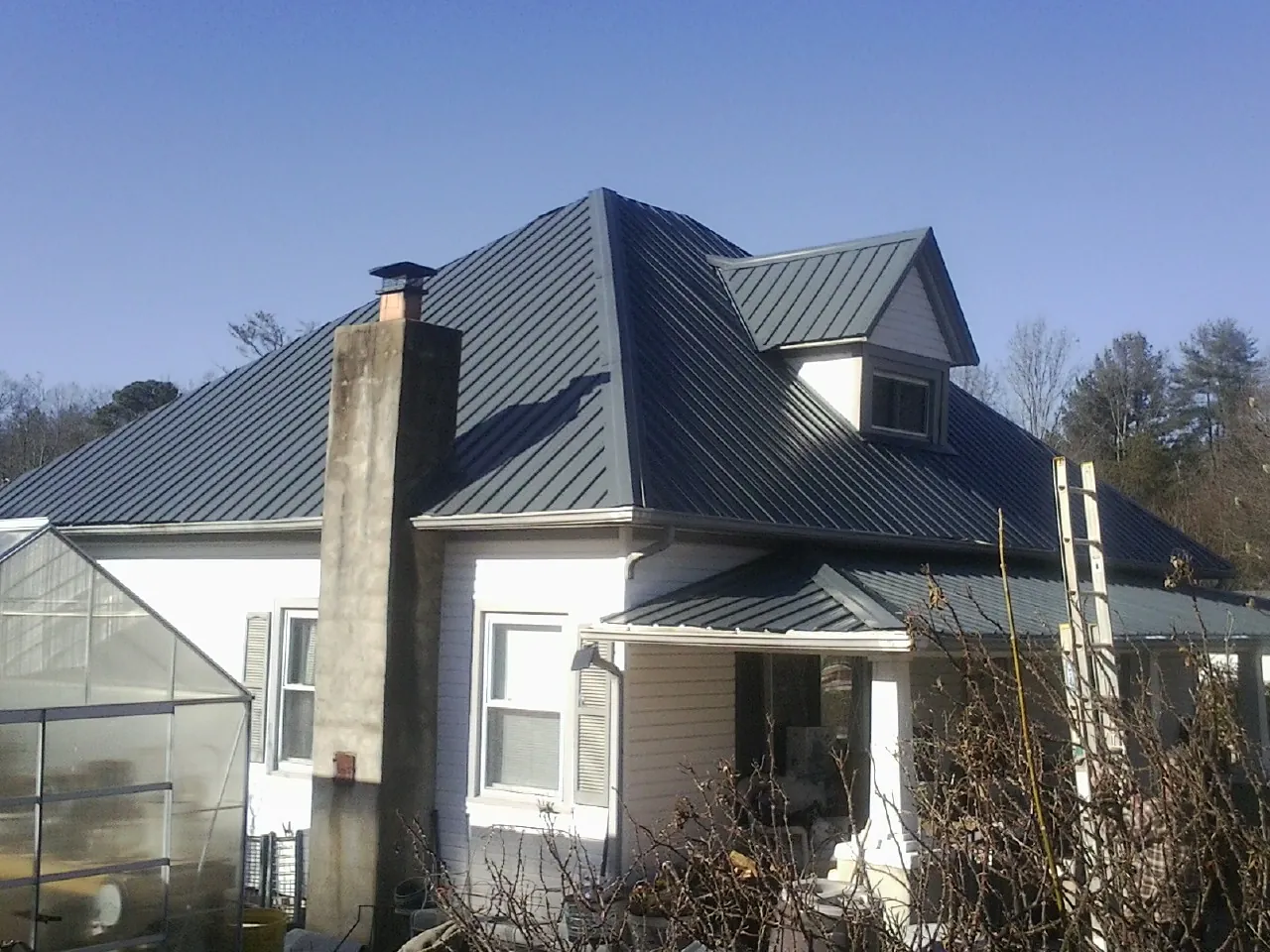 Dark blue standing seam metal roof on a white farmhouse with dormer — Slate & Tile Roof Repair by Roofing Brothers in Fromberg