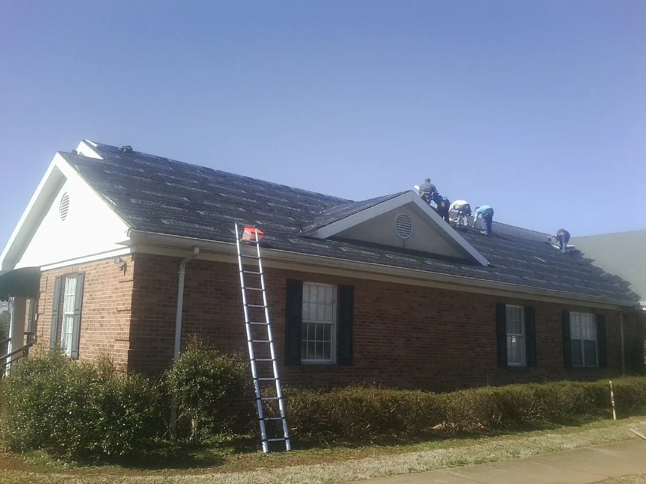 Crew tearing shingles off a brick ranch roof with a ladder set — Emergency Roof Repair work by our crew in Fromberg