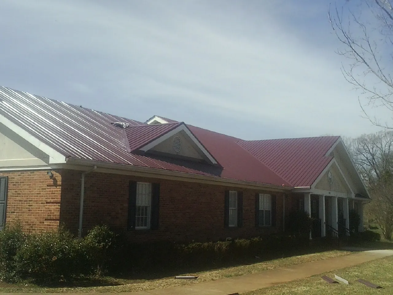 Red metal roof with gabled entries on a long brick building, from a Hail Damage Roof Repair job in Fromberg