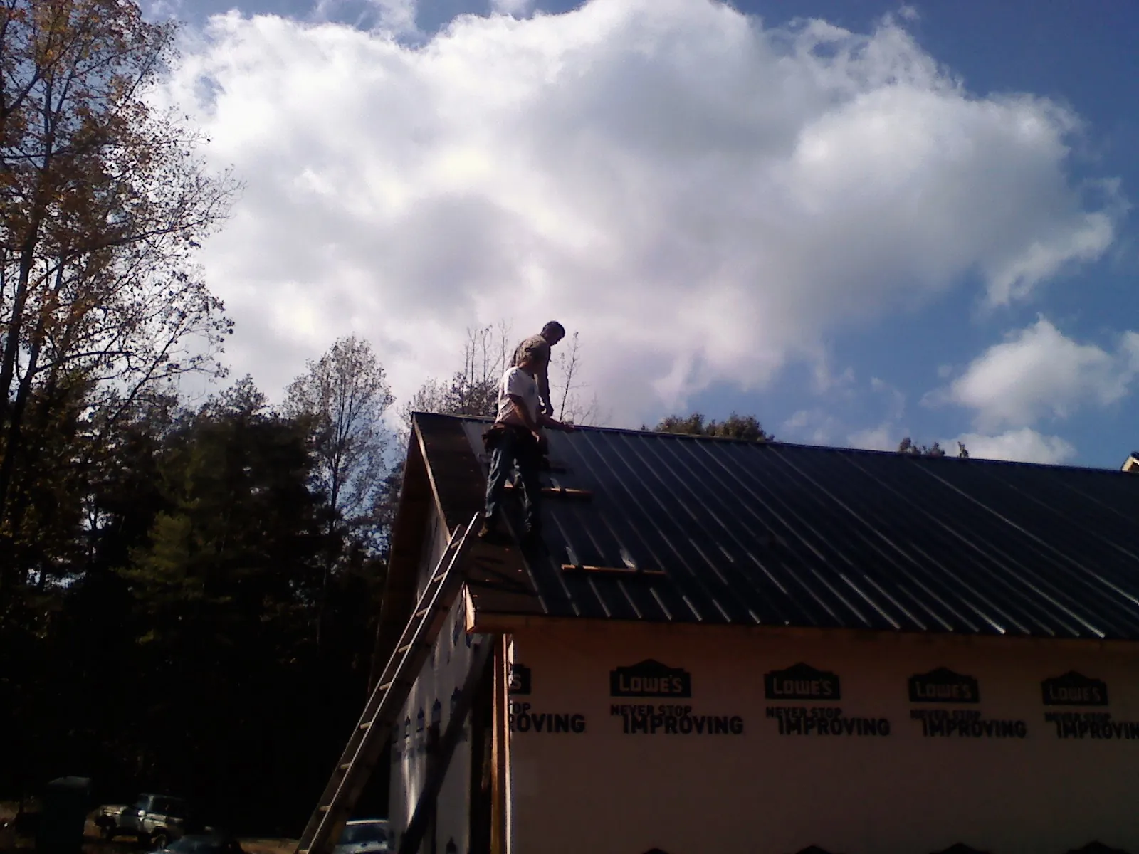 Roofer fastening dark metal panels high against a cloudy sky, from a Roof Inspection job in Fromberg